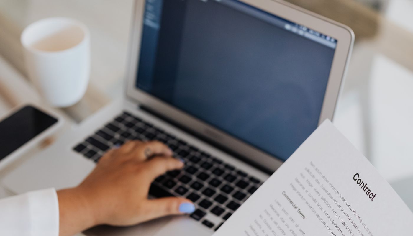 Person reviewing a printed document beside a laptop